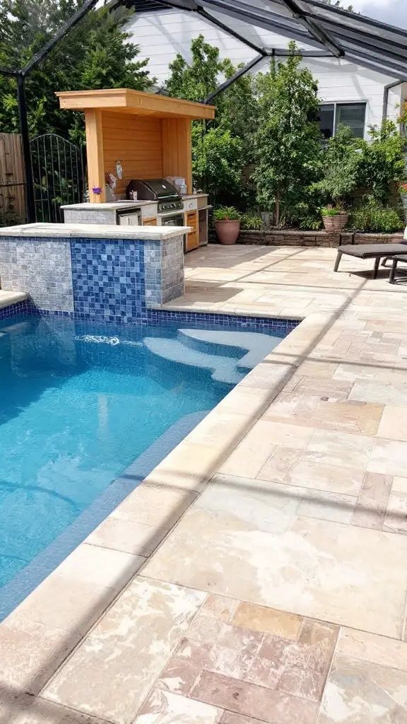 A small backyard pool with a swim-up bar and outdoor kitchen surrounded by greenery