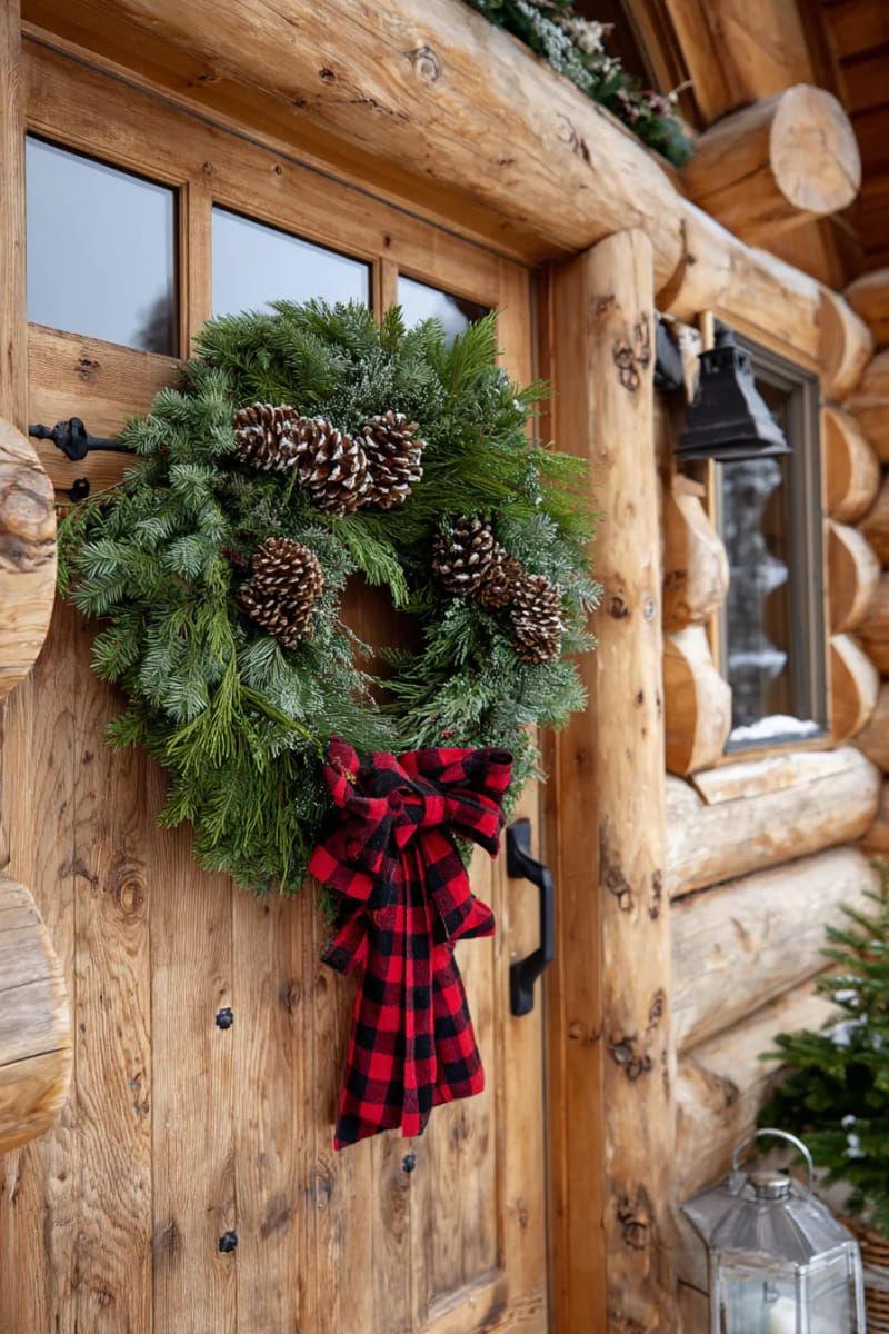 oversized rustic wreath with pinecones and buffalo plaid ribbon on log door 1